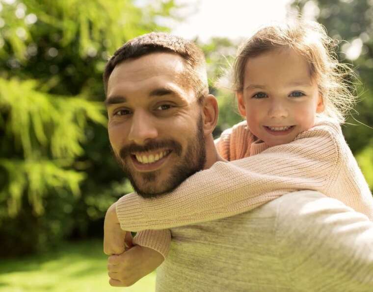 Father hi carrying daughter on back and smiling