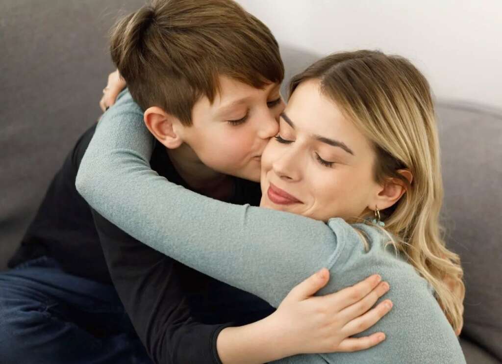 son is hugging and kissing his mother's cheek.
