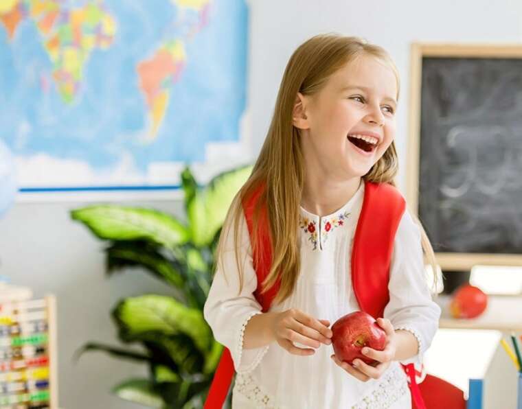 The girl is laughing and after going to school, entering into the classroom.