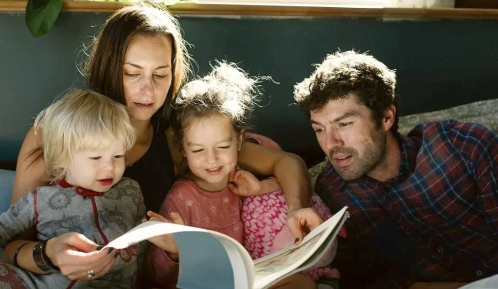 mother and father along with children reading something from book and spending quality time