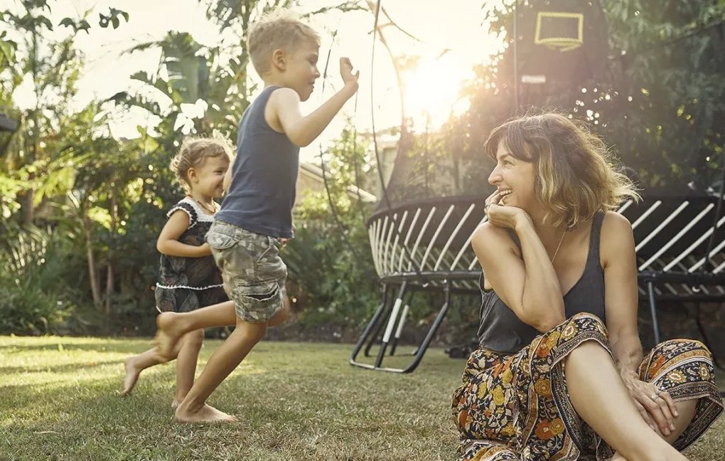 children are playing in the ground and mother is smiling at children