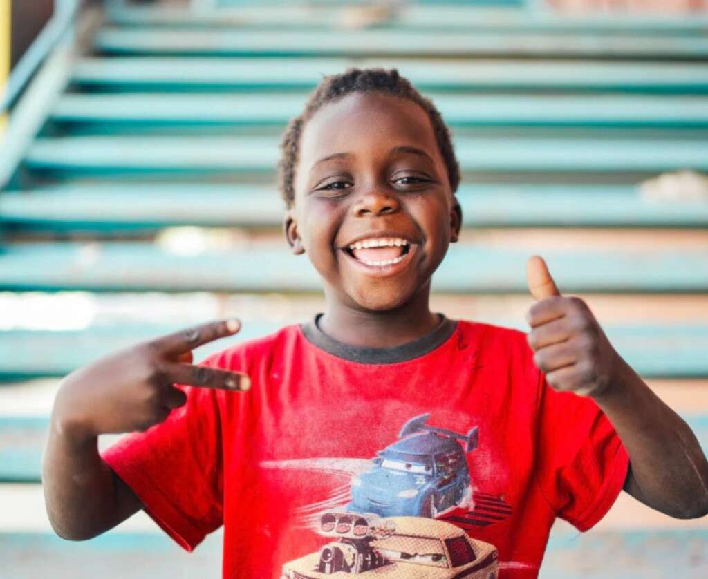 black boy wearing red shirt smiling and giving a thumbs up