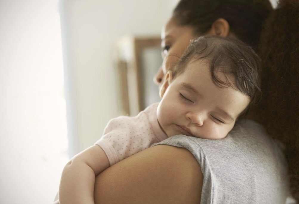 baby is sleeping on mother's shoulder